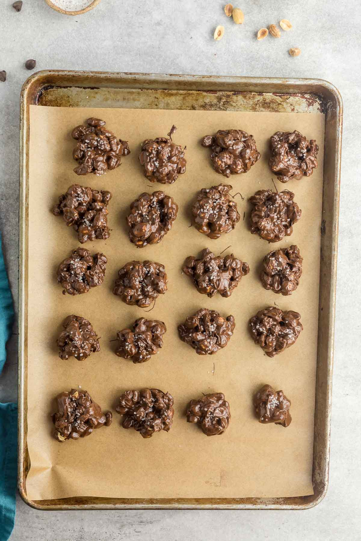 chocolate peanut clusters topped with sea salt on parchment paper baking sheet