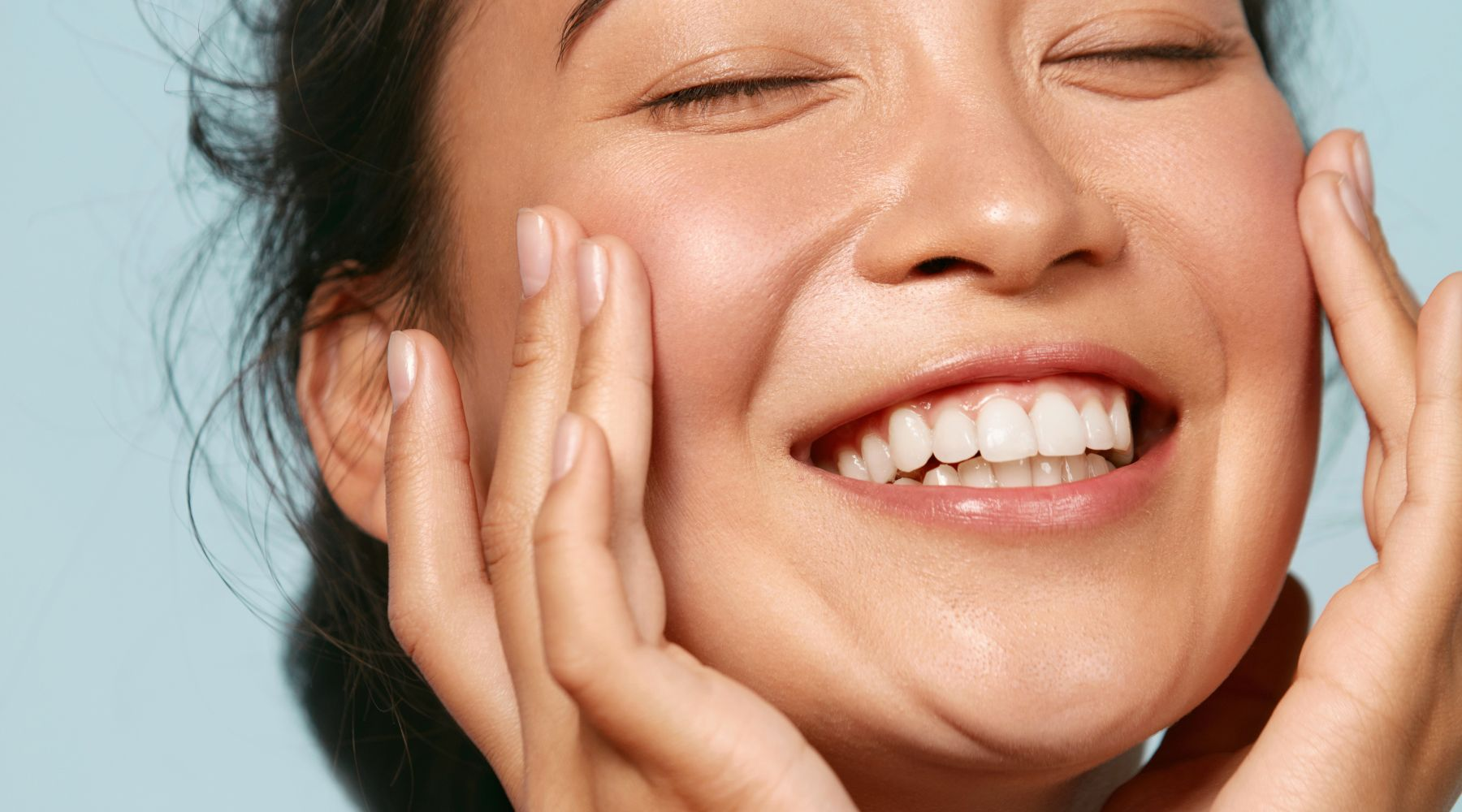 Woman in blue top laughing and touching her cheek lightly