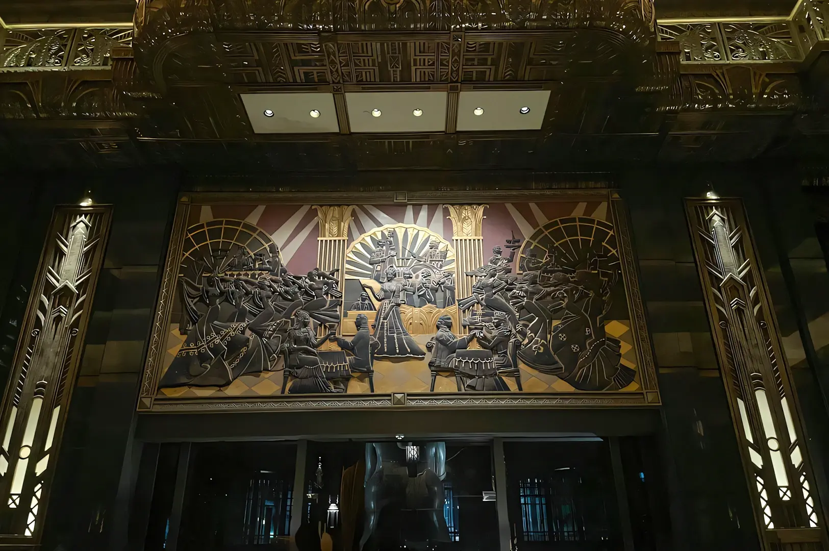 Straight‑on eye‑level shot of an Art Deco–style wall mural inside Atlas Bar Singapore, featuring sculptural figures, geometric patterns, and dramatic lighting above the entrance area.