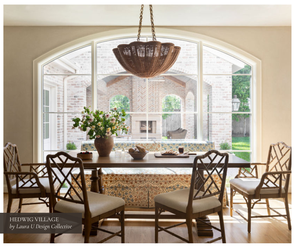 Sunlit breakfast room with natural wood Chippendale chairs, an antique-style pendant chandelier, and a view through arched windows to an outdoor fireplace and patio beyond, blending classic charm and comfort.