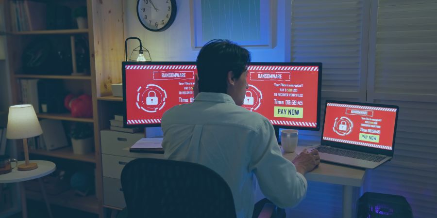 man sitting at a desk in front of 3 screens showing a ransomware alert