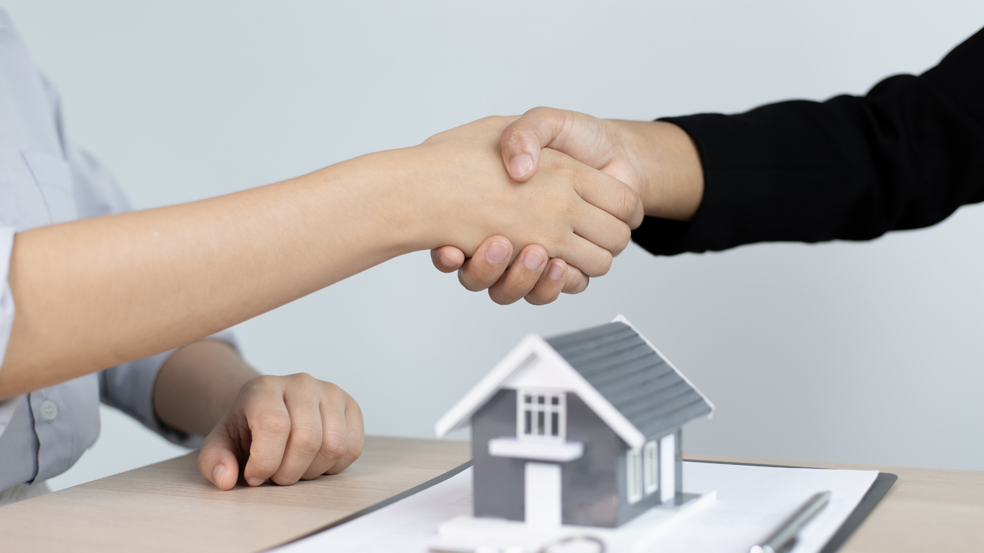 two people shaking hands over a model of a house
