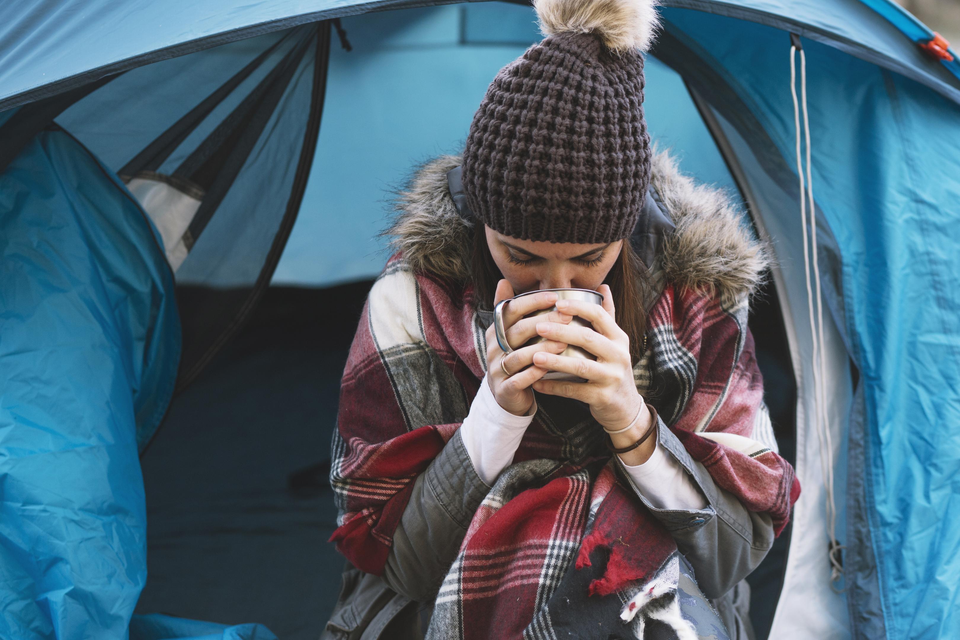 a woman drinking a hot drink outside her tent