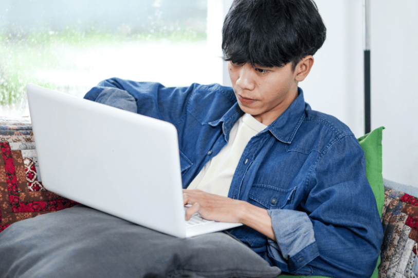 A young person focused on a laptop while relaxing on a sofa, representing a potential customer in Singapore searching for restaurant reviews and dining recommendations online.