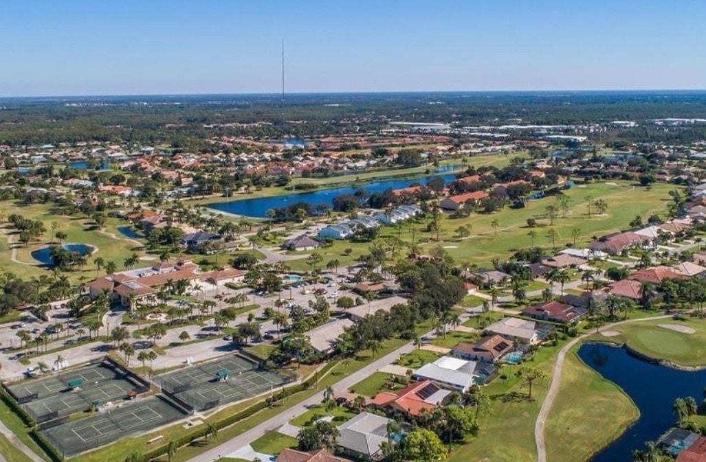 An aerial view showcases the prestigious Spanish Wells golf course community in Bonita Springs, Florida, featuring luxury homes with stunning lake and golf course views. The beautifully designed pool home is surrounded by perfectly manicured greens, embodying the incredible Florida lifestyle.