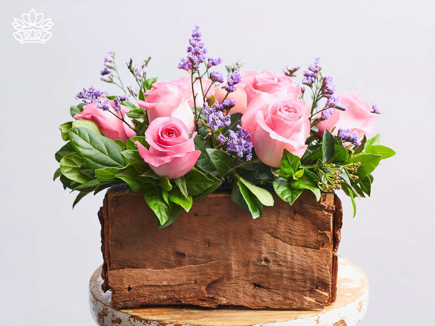 A rustic wooden box overflows with lush greenery and an arrangement of delicate pink roses and lavender flowers, embodying thoughtful gifts and natural beauty. Fabulous Flowers and Gifts. Gifts for Her.