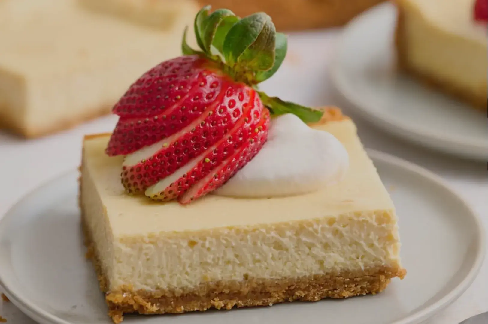 A slice of cheesecake topped with a strawberry and whipped cream on a plate.