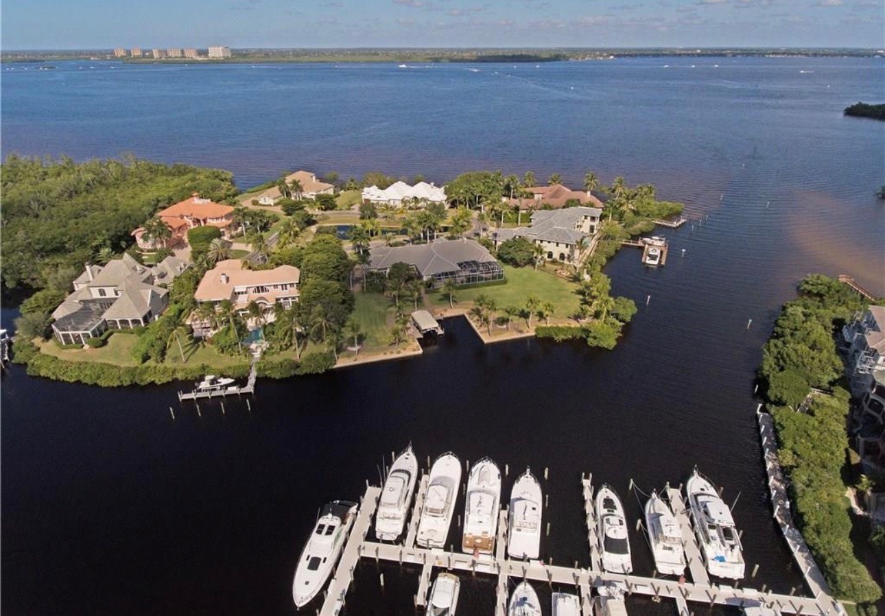 The image depicts an elegant waterfront restaurant terrace in Fort Myers, featuring outdoor dining with views overlooking the marina and beautifully secluded natural harbor. Guests enjoy a relaxed atmosphere, perfect for social events while surrounded by the scenic waterways and yachts.