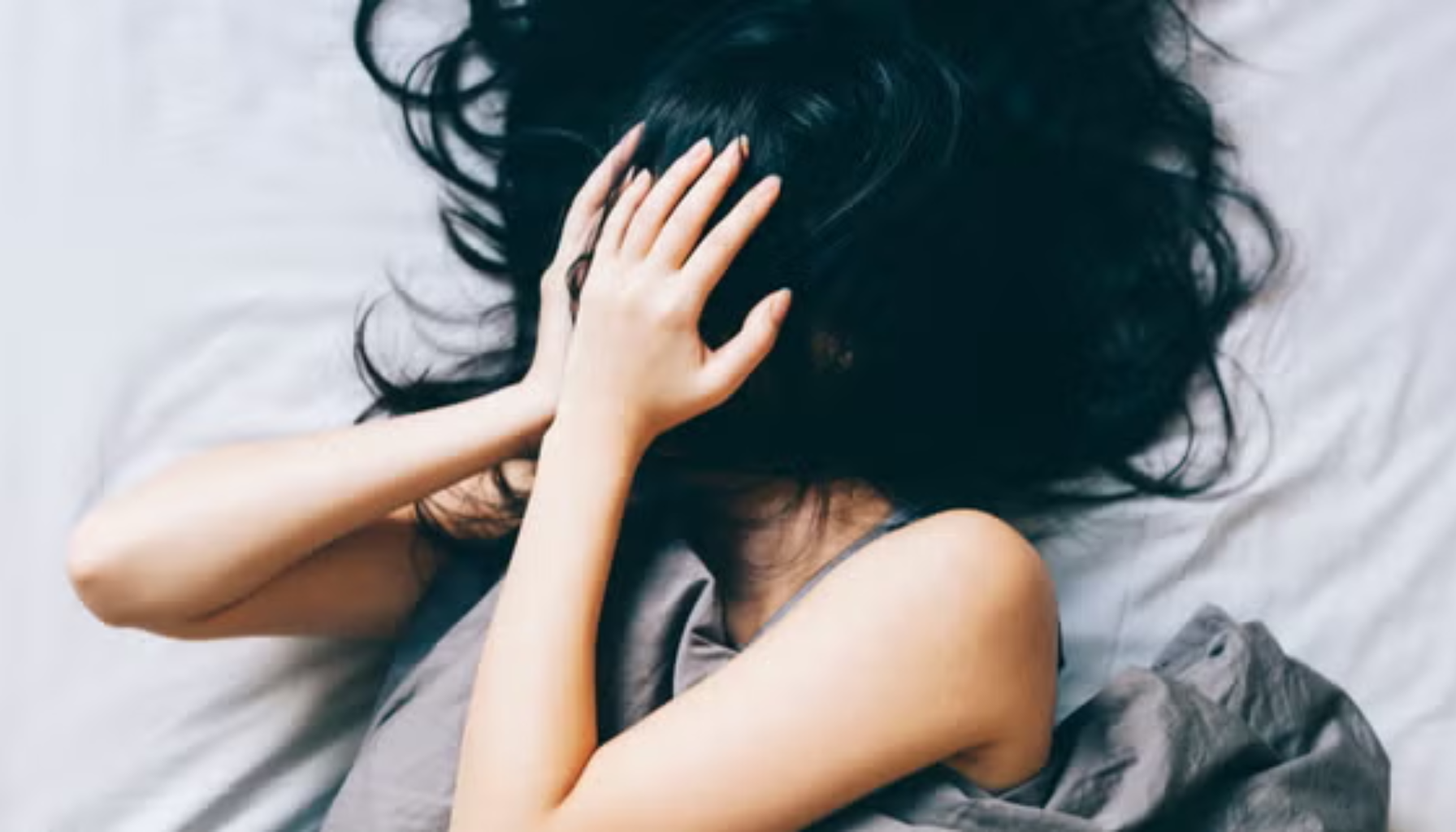 "Kvinne ligger i seng med hånden foran ansiktet, ser ut til å være stresset eller opprørt."
