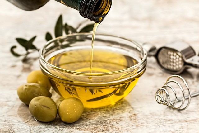 An image of a bowl of olive oil with olive oils beside it on a table. 