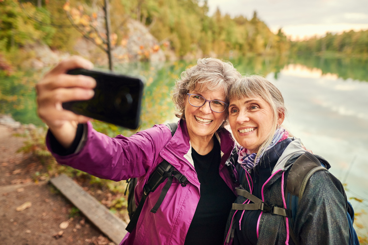 Two mature women in jackets snapping a selfie on a hike. 