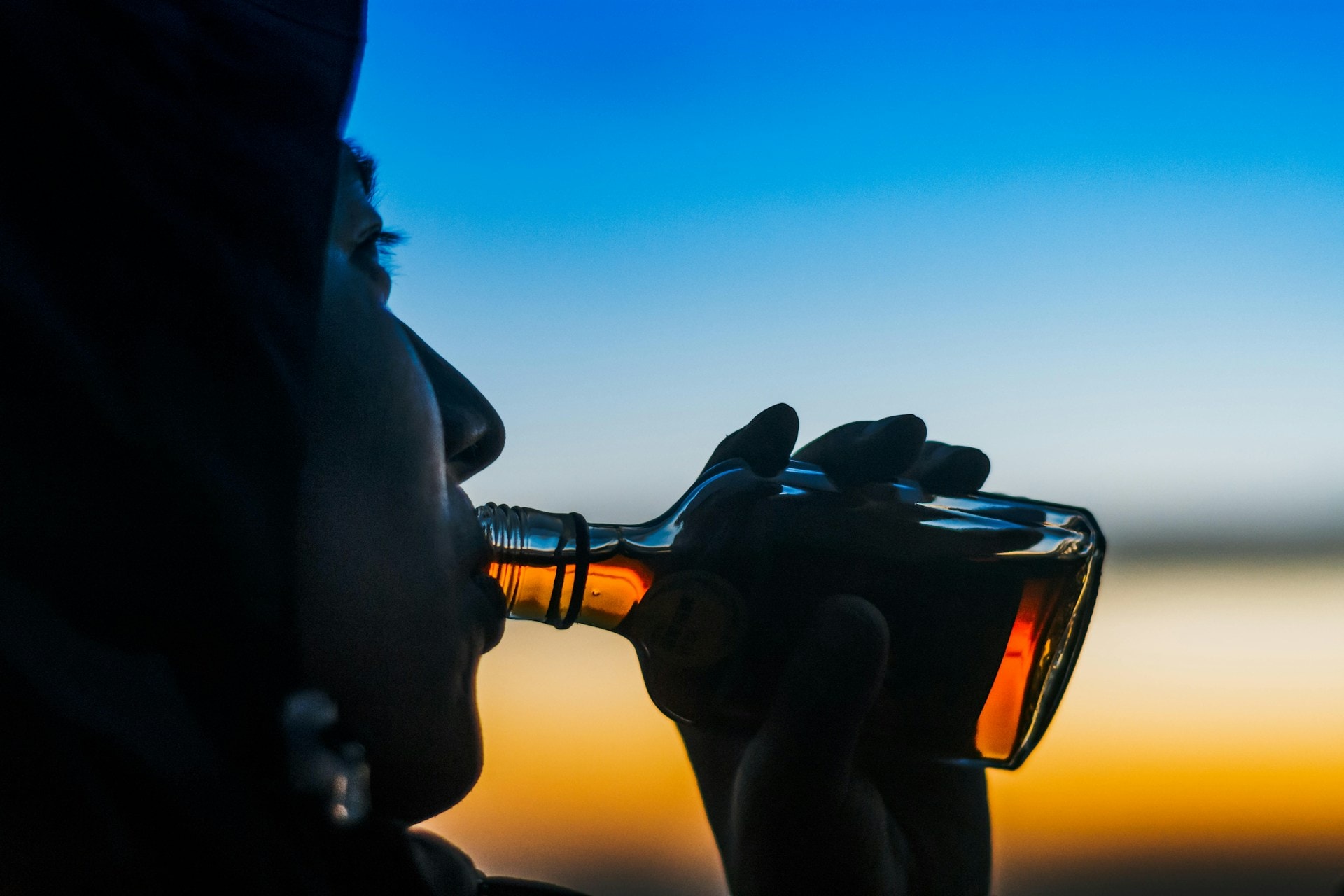 A moody aesthetic photo of a guy in a hoodie drinking straight whiskey from the bottle during sunset - https://unsplash.com/photos/person-drinking-liquor-in-clear-glass-bottle-2jzy-VfhI04