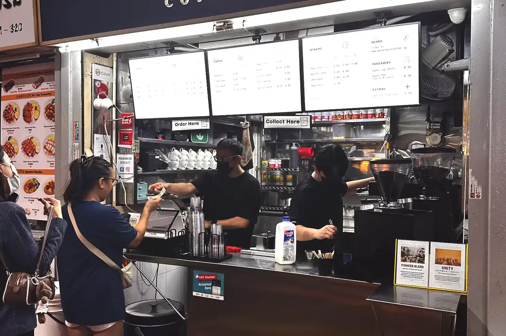 A customer paying a barista at the counter of Generation Coffee, with espresso machines, coffee beans, and pricing signs visible on display.