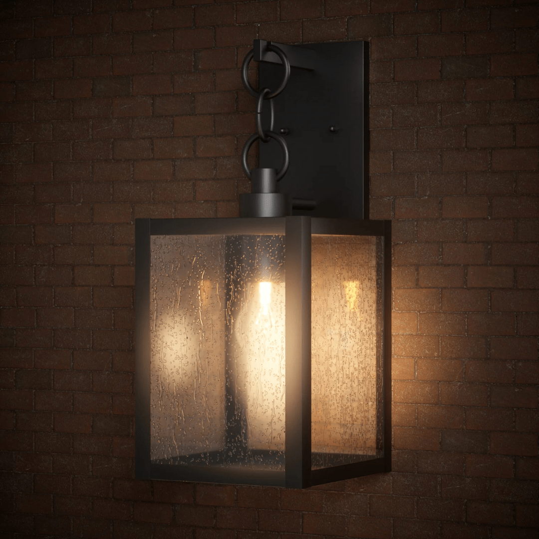 Modern black outdoor wall lantern with clear seeded glass panels and a glowing bulb, mounted on a brick wall.