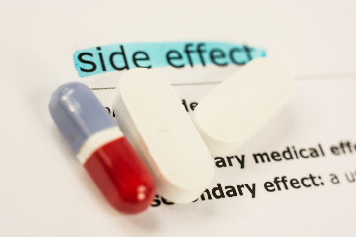 Medicine capsule and tablets over a document about drug side effects