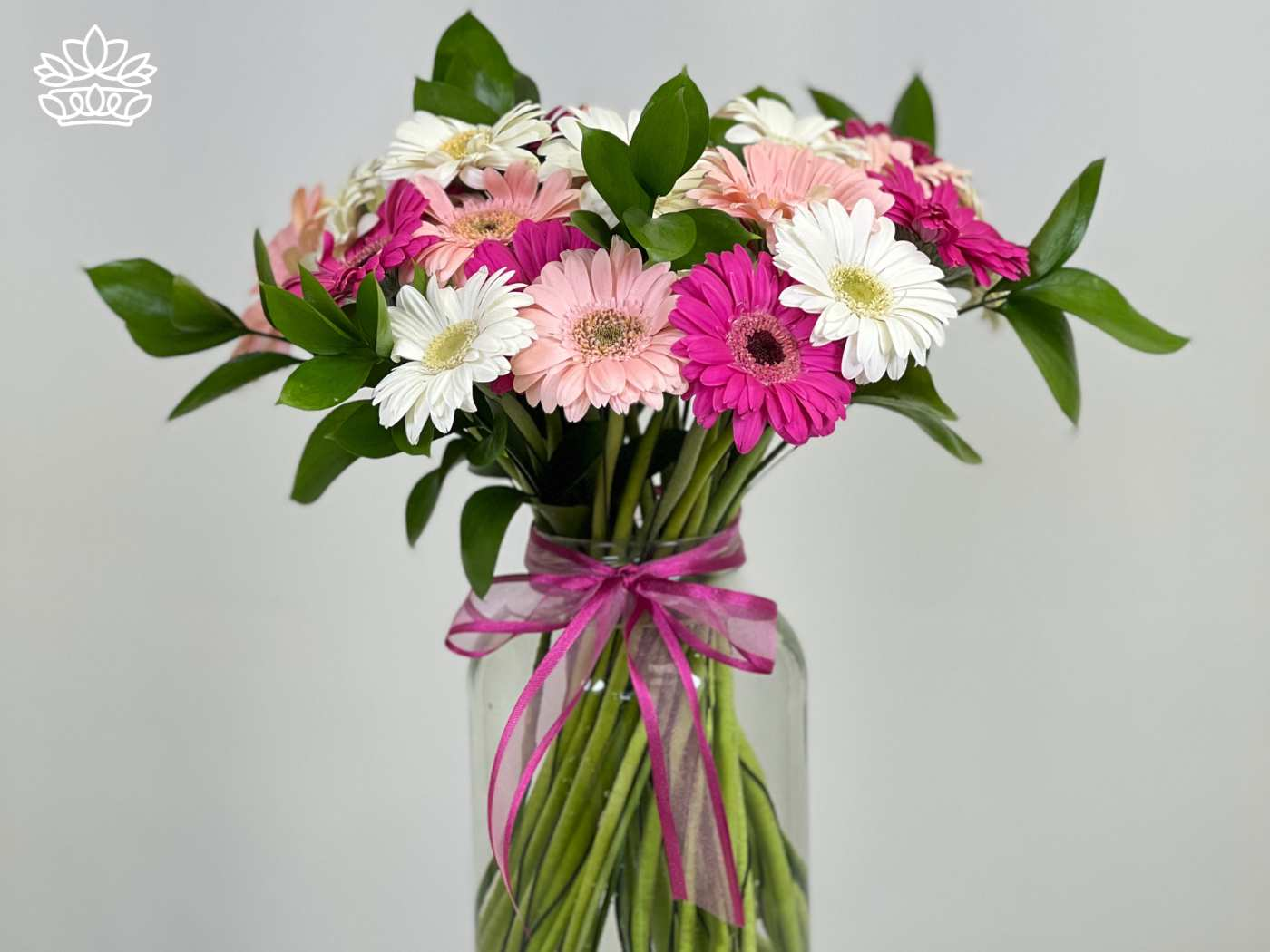 A bouquet of pink, white, and light peach Gerbera daisies, arranged with green foliage in a clear vase, tied with a pink ribbon. Fabulous Flowers and Gifts. Gerberas Collection. Delivered with Heart.