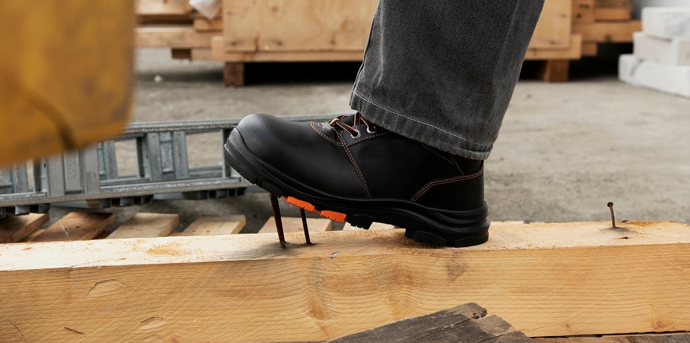 Снимка на крак обут в работна обувка, който стъпва върху стърчащ пирон