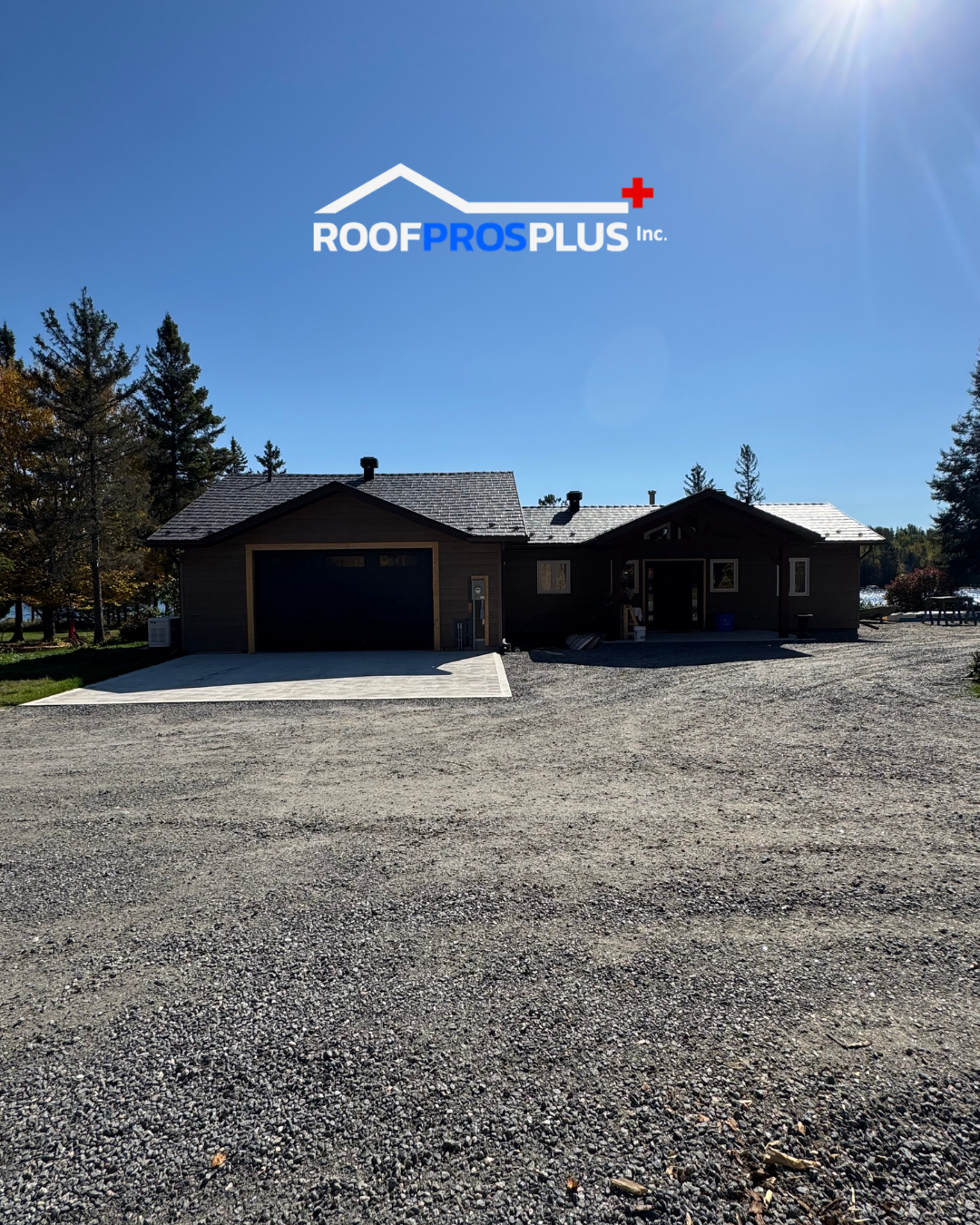 Single-storey modern home with a dark metal roof, garage, and surrounding trees under a clear blue sky. Roof Pros Plus logo appears above the home