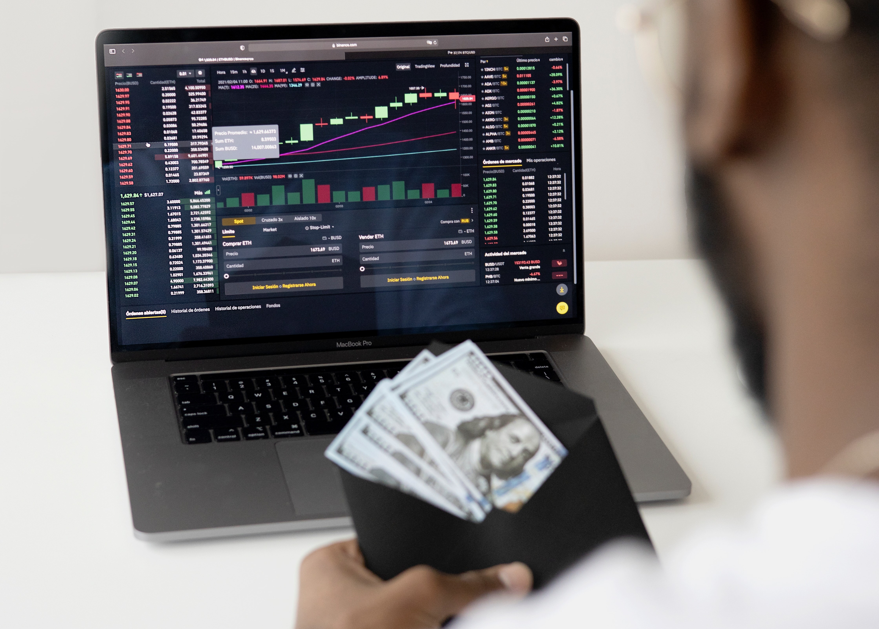 A person holding a envelope with money it and they are sitting in front of a stock chart, on a screen.