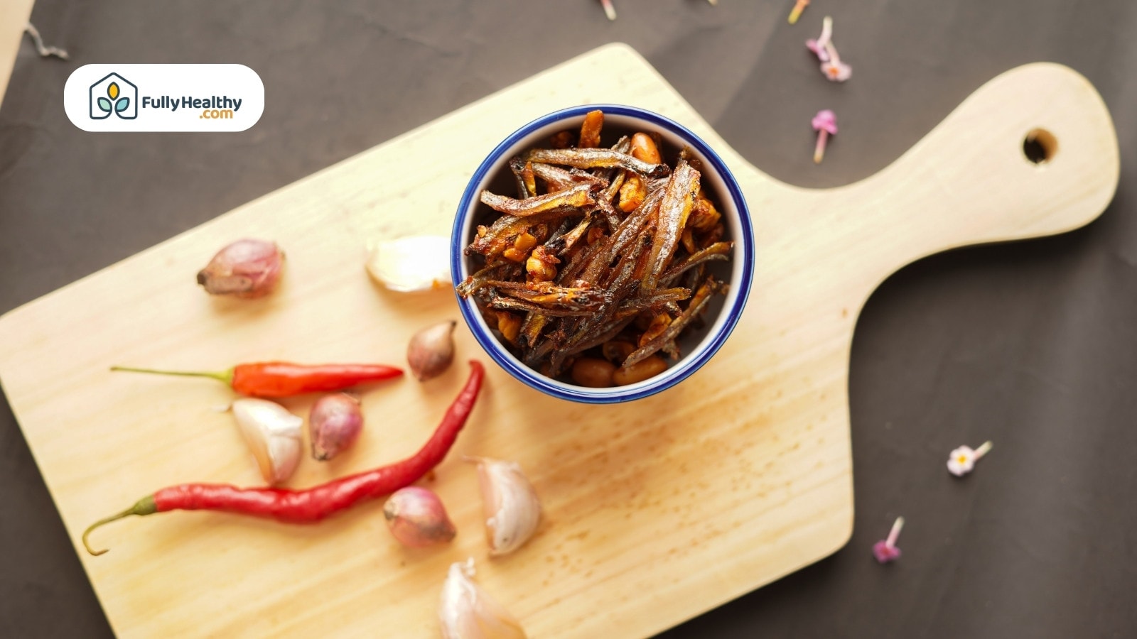 Bowl of fried anchovies with garlic and chili on wooden board