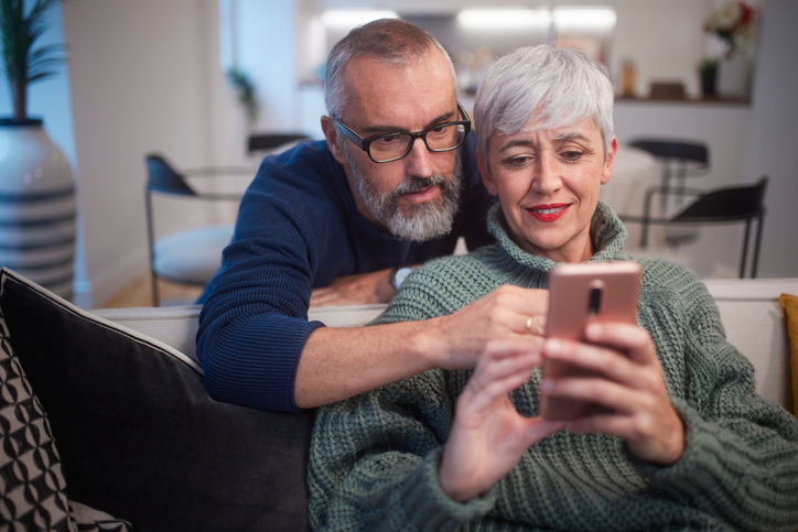 Gray haired couple hugging and looking at a cell phone.