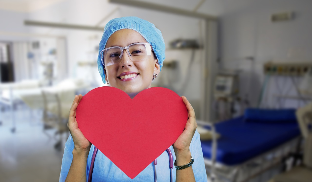 An image of a nurse holding a large cardboard heart in front of her body. 
