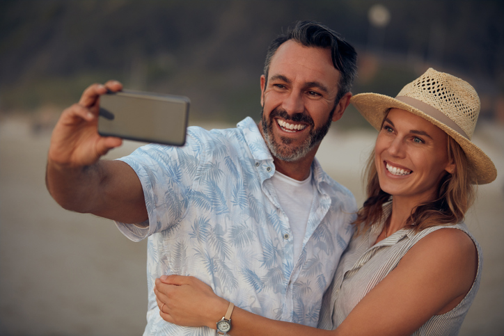 Happy couple hugging and taking a selfie on the beach.