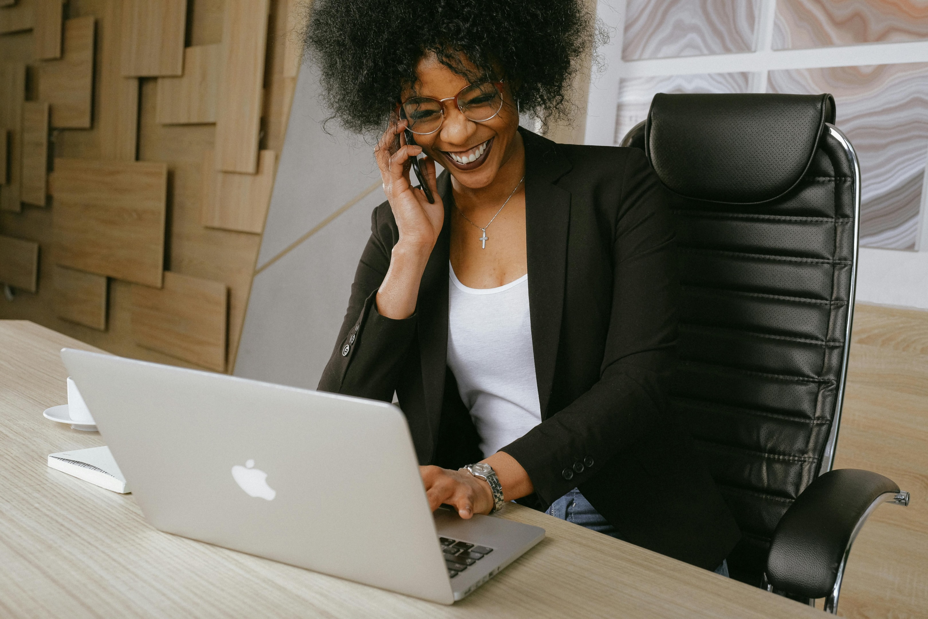 A woman smiling while on the phone and sitting behind her laptop computer working remotely.