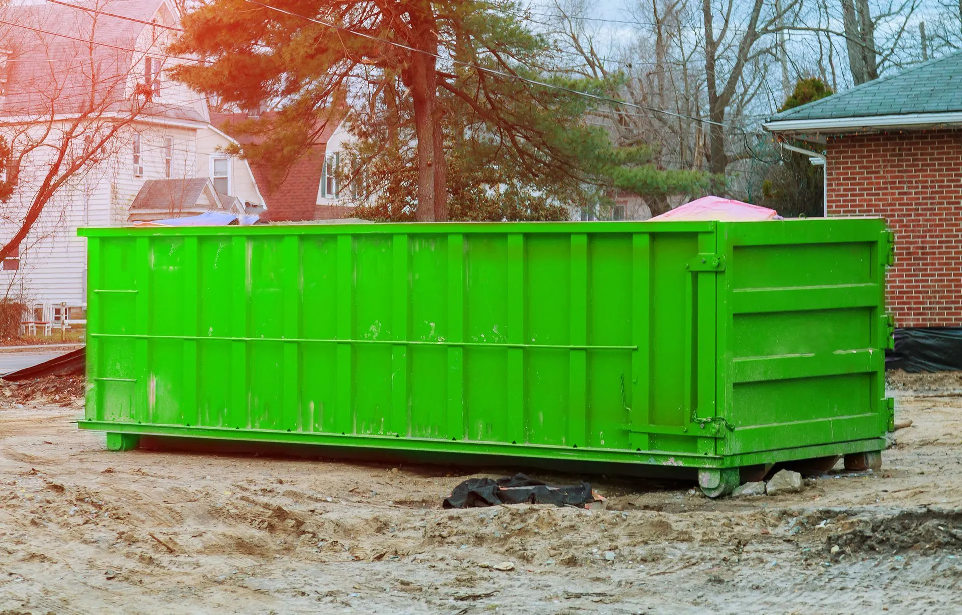 A green dumpster in a dirt lot