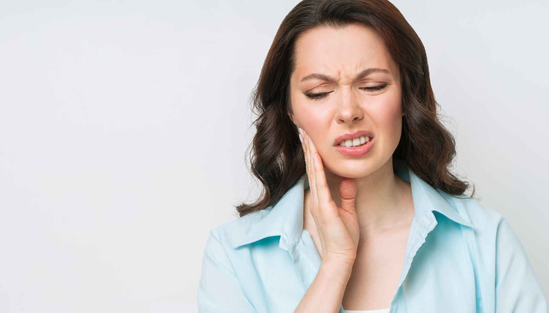 Kvinne med smertefullt ansiktsuttrykk som holder hånden mot kinnet, tydelig preget av tannverk eller kjevesmerter.