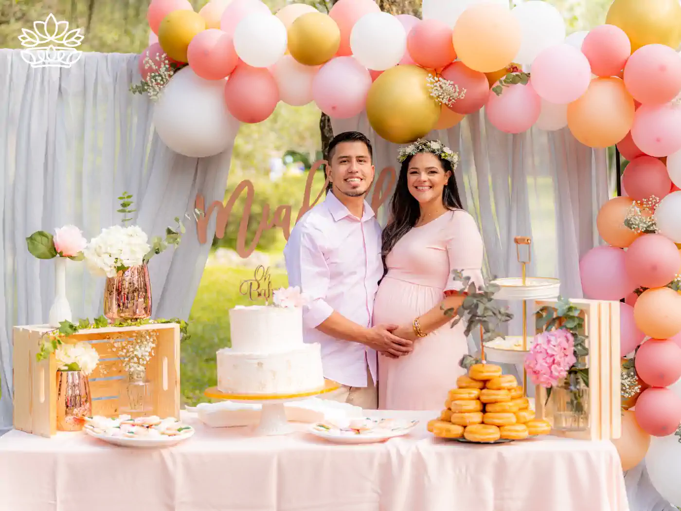 A happy couple at a baby shower, standing by a beautifully decorated table with a cake, flowers, and balloons in pastel colours. Fabulous Flowers and Gifts: Baby Shower Flowers Collection