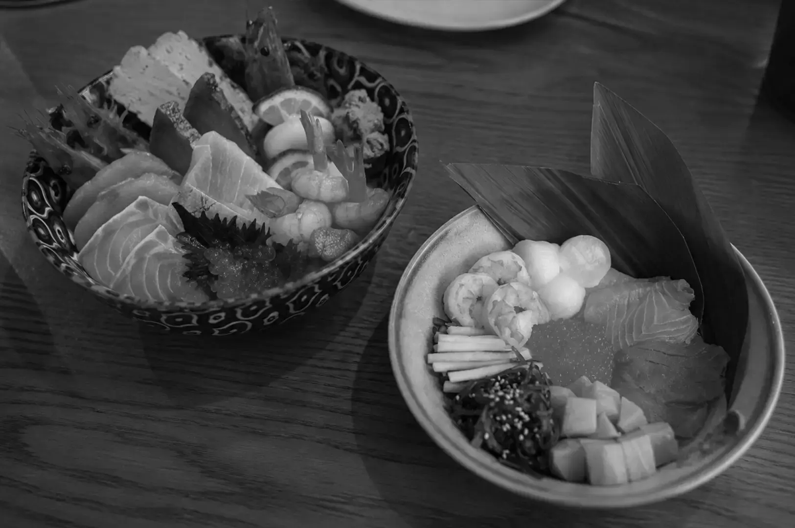 wo Japanese chirashi don bowls featuring assorted sashimi, shrimp, ikura, tamagoyaki, and fresh seafood over rice.