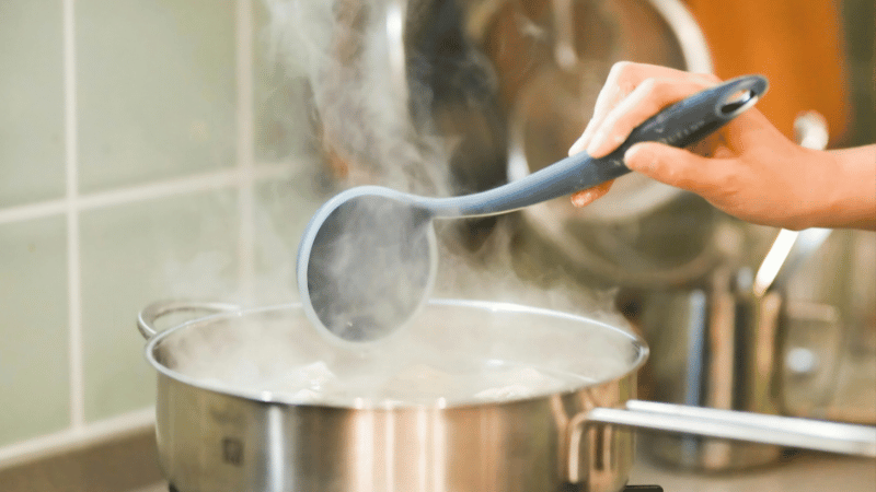 A woman is using nylon cooking utensils to stir soup.