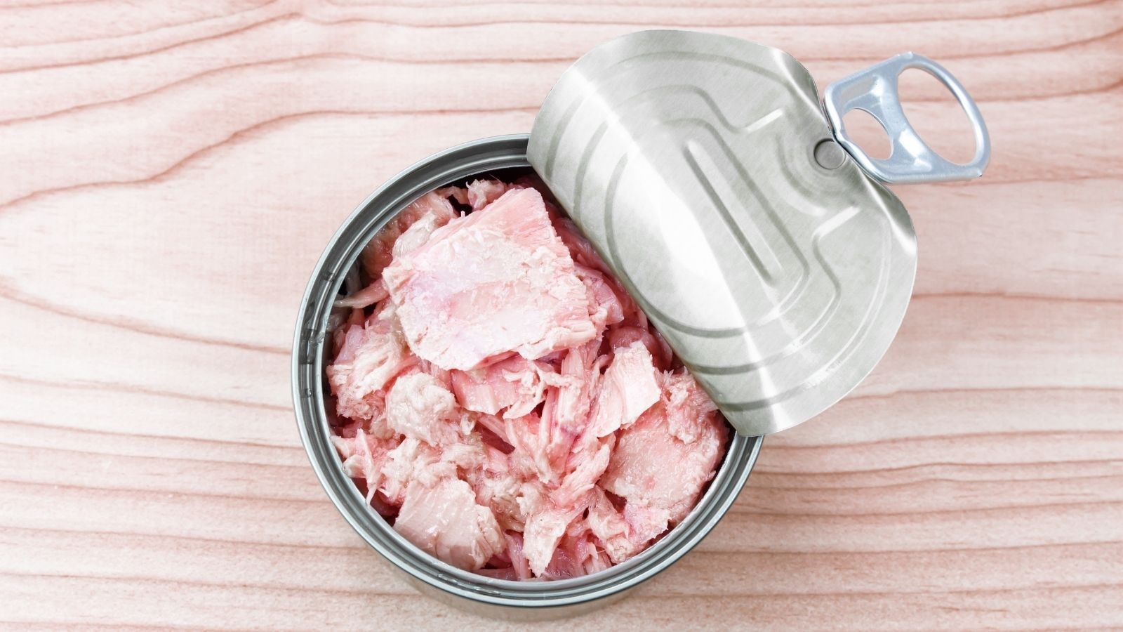Open can of solid white albacore tuna on wooden surface
