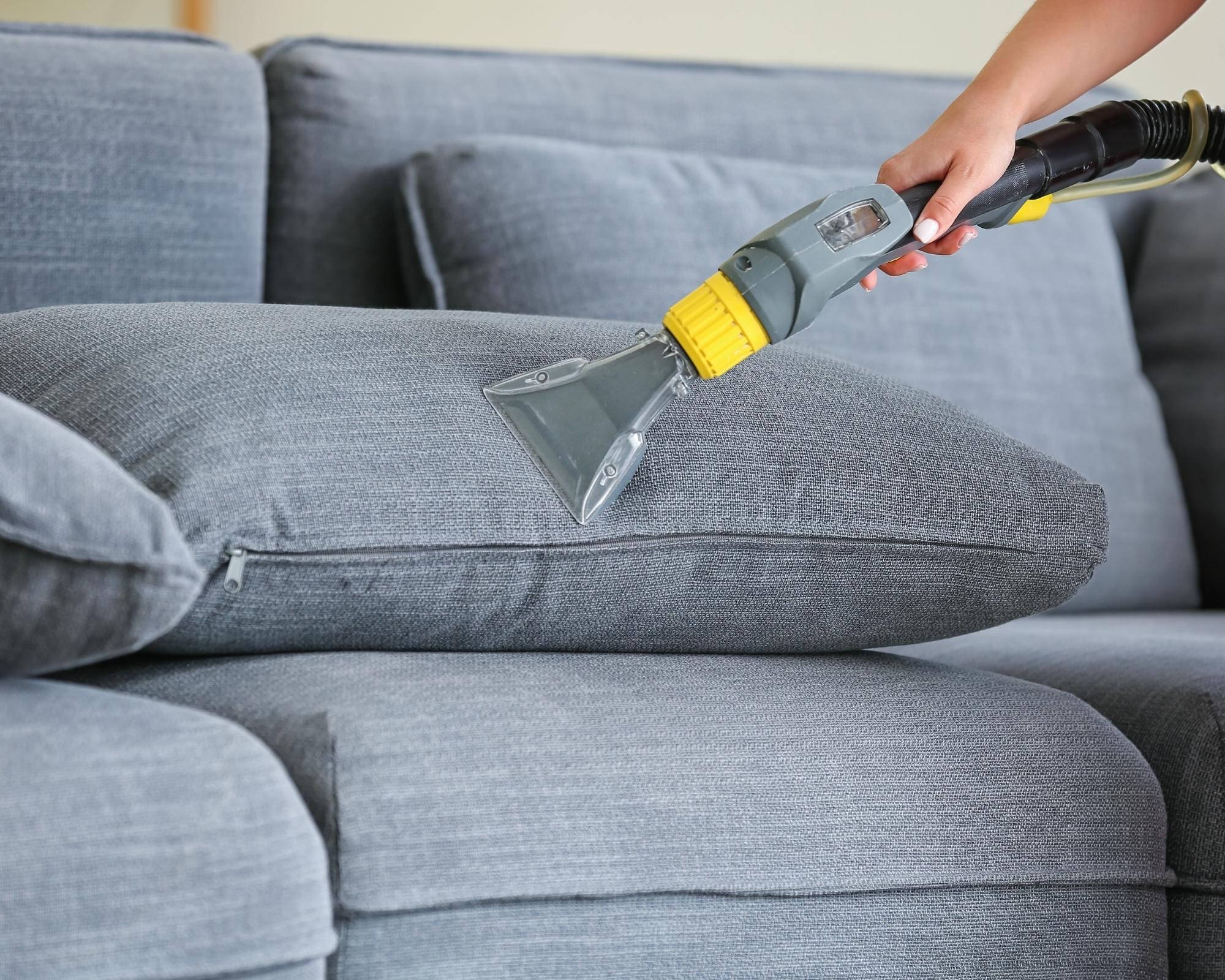 Professional sofa cleaning in progress on a dark grey fabric couch using an upholstery cleaner by Cleanology SG, demonstrating effective deep cleaning methods to refresh and sanitize sofas in Singapore.