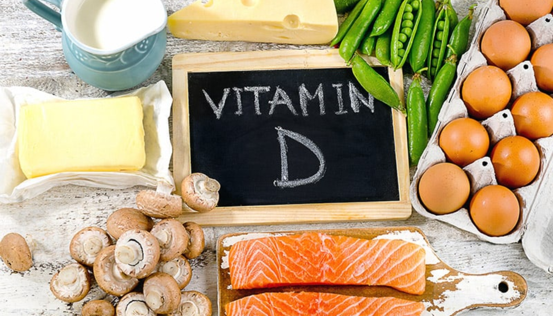 Mangel på Vitamin D: Overraskende Effekt På Tennene Dine 18 Matvarer rike på vitamin D, inkludert egg, laks, melk, ost, smør, sopp og erter rundt tavle med teksten "Vitamin D".