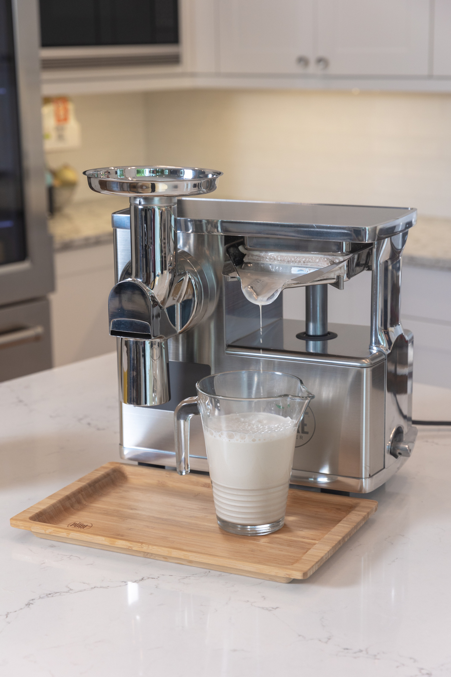 A glass pitched of homemade almond milk stands under the press of the PURE Juicer.