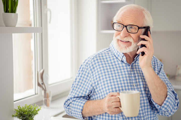 Older man with white hair and glasses having coffee and talking on his cell. 