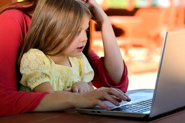 A little girl sitting on her mother's lap while looking at a laptop.