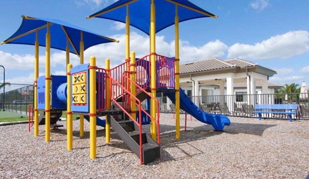 The image shows the entrance to the Portico community in Fort Myers, featuring a stylish gate house surrounded by lush landscaping with palm trees and tropical plants, welcoming residents into this highly desired gated community. This picturesque setting reflects the natural beauty and contemporary design that characterize the exquisite modern luxury of Portico real estate.