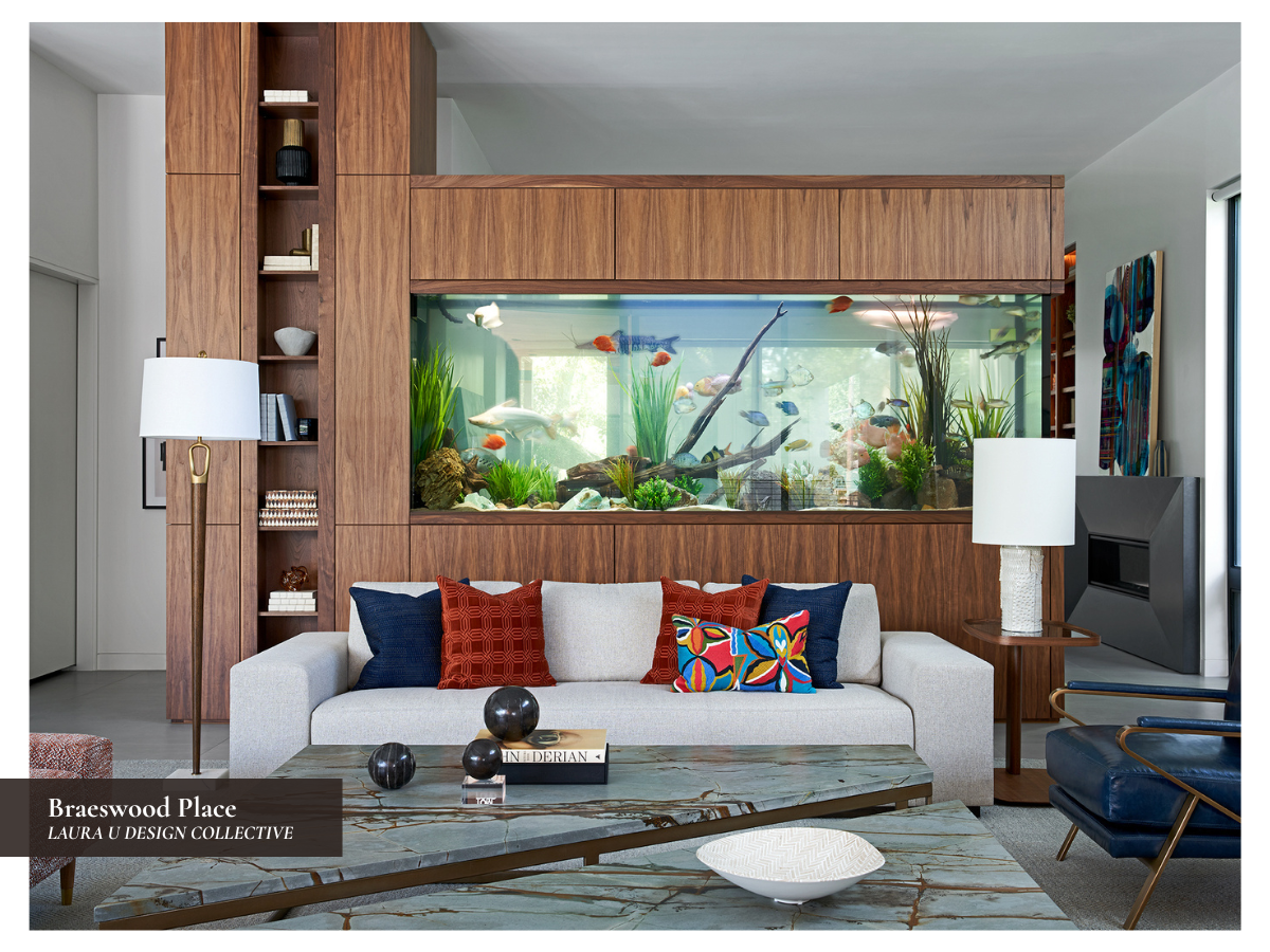 Modern living room at Braeswood Place featuring a built-in aquarium wall, walnut millwork, blue accent chairs, and rust-colored pillows.