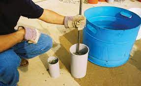 A technician using a tamping rod to make two equal layers of concrete mix in a cylinder mold