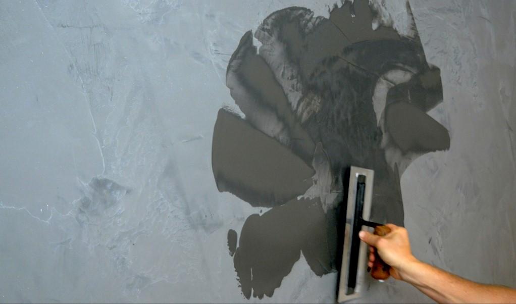An artisan is skillfully applying lime plaster to a smooth wall using a stainless steel trowel, showcasing the meticulous technique required for achieving a polished marble-like finish. This traditional application process highlights the beauty of natural materials, as the layers of marmorino and venetian plaster create a refined, reflective surface that enhances the elegance of the space.