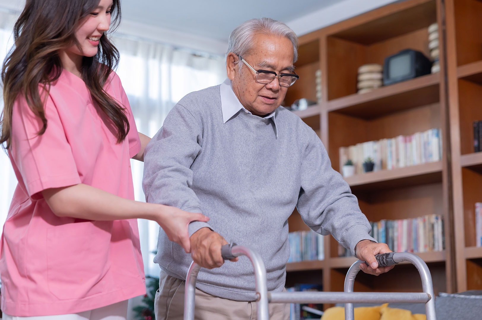 Caregiver assisting an elderly man walking with a walker.