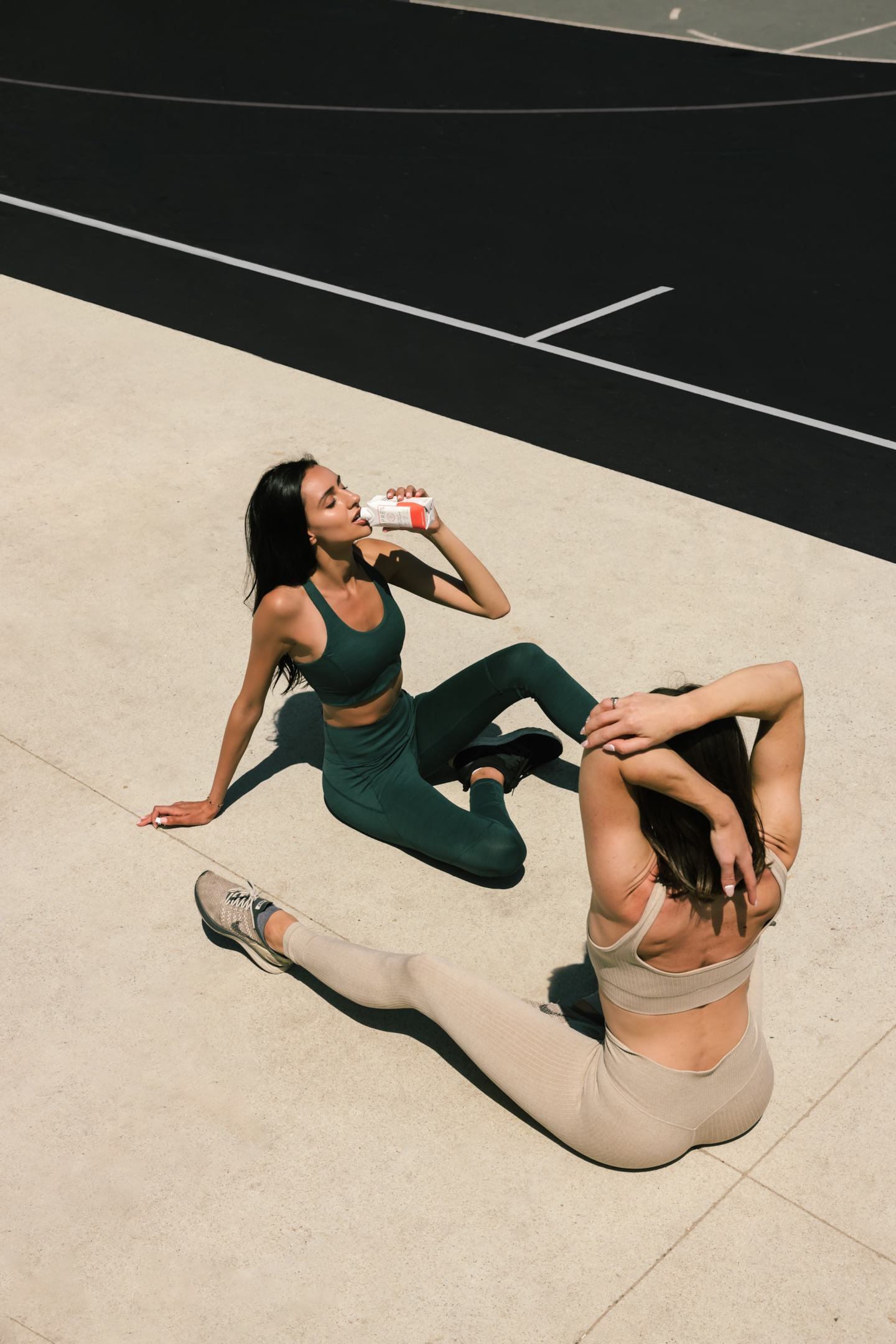 Mulheres se alongando, enquanto uma bebe um suplemento pronto para consumo. Foto de Tyler Nix, Unsplash.