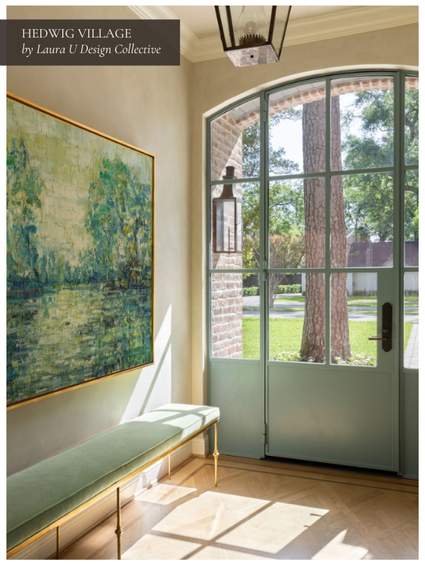 A bright entryway with a large landscape painting in green and blue tones, a pale green upholstered bench, and a glass-paneled door that lets in abundant natural light.