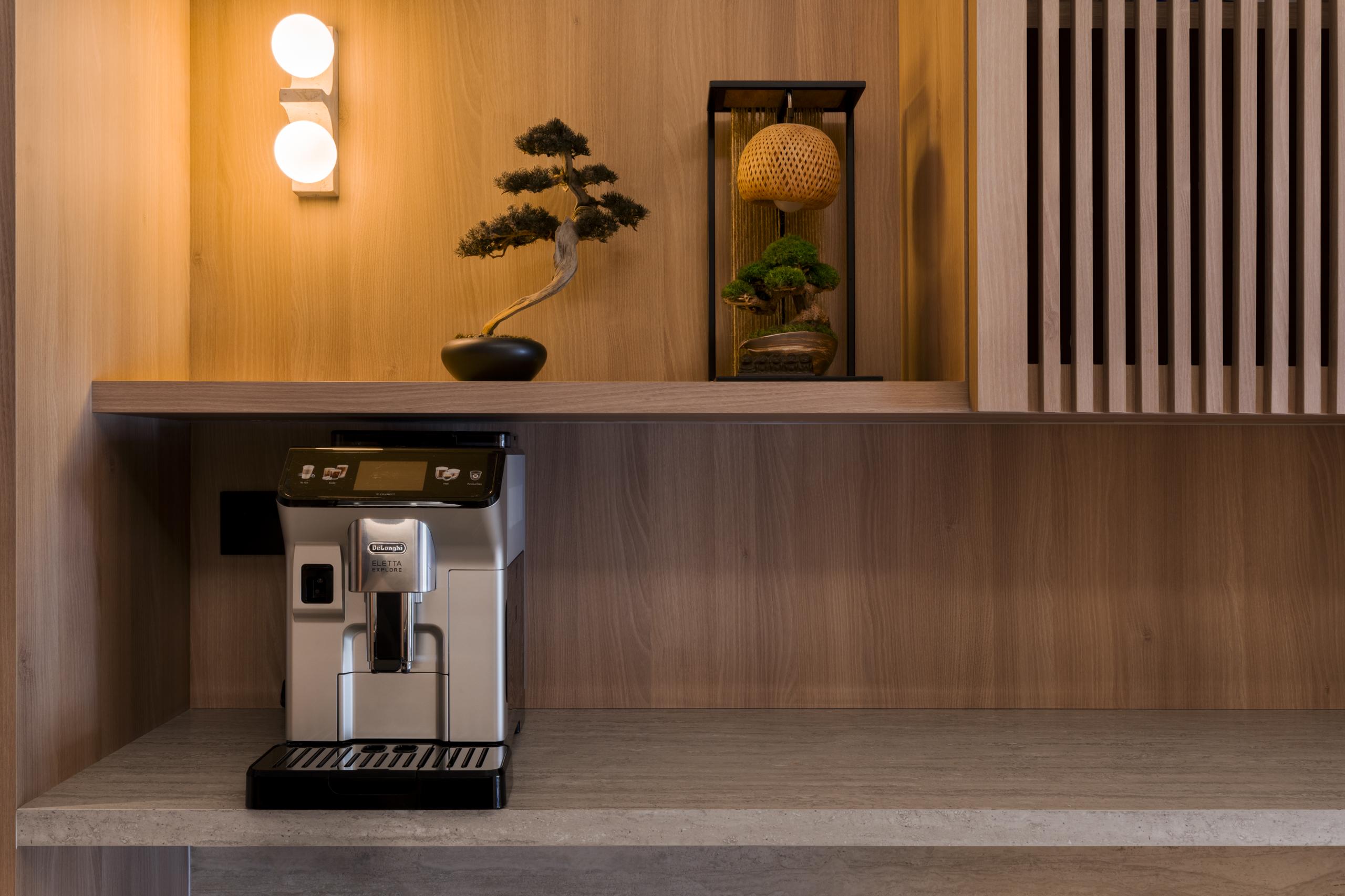 Modern Japandi coffee nook featuring wood paneling, a bonsai tree, and a built-in espresso machine under warm orb lighting.