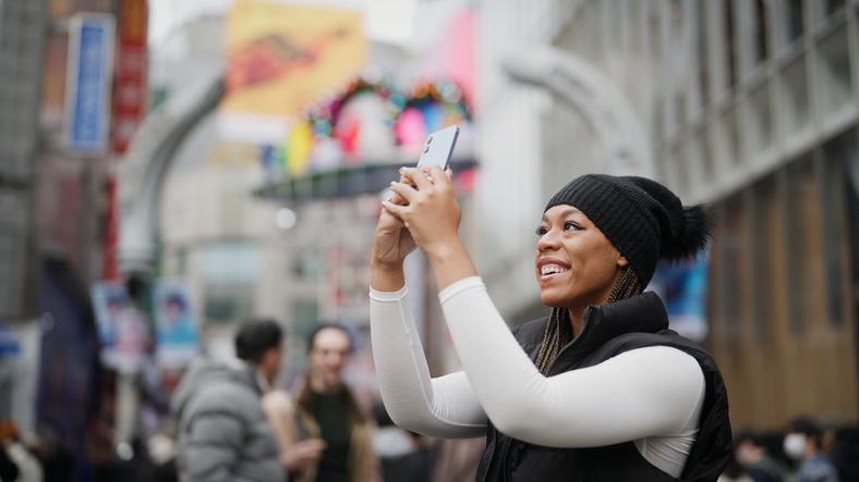 Happy young woman in a black cap taking a photo with her cell phone. 