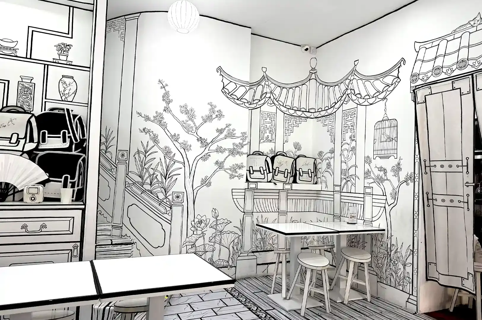An interior corner of Cafe Monochrome featuring intricate 2D illustrated murals of traditional Chinese architecture, a bridge, and cherry blossom trees.
