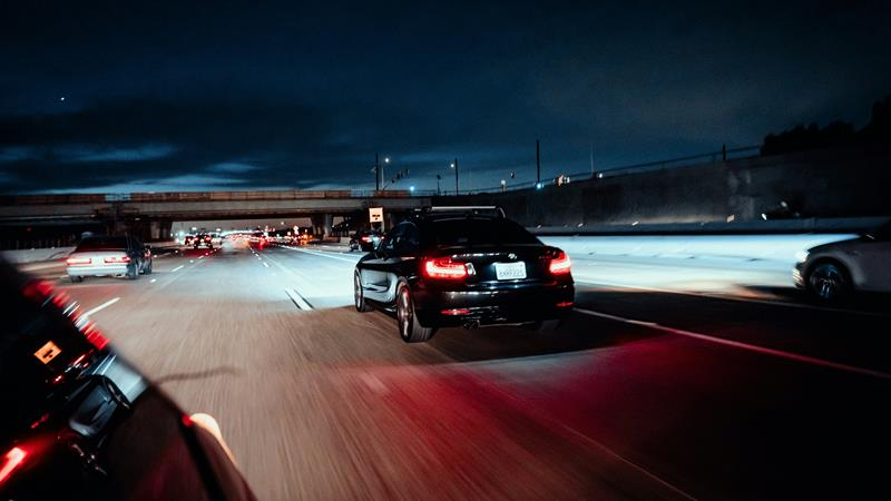 Black car driving down highway with bright headlights